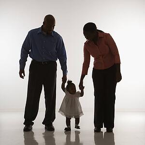 Man and woman standing holding up infant girl by her hands against white background
