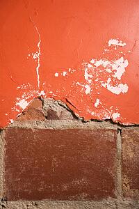 Red wall with cracking plaster and brick