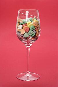 Wine glass full of colorful candy hearts with sayings on them on red background