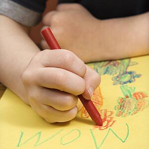 Boy drawing on yellow paper with crayons