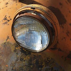 Close-up of headlight on scratched up rusty old pick-up truck