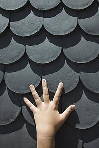 Close-up of boy's hand on rooftop with scale shaped shingles in Lisbon, Portugal.
