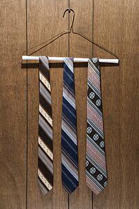 Three retro ties hanging on a wire hanger against wood paneling