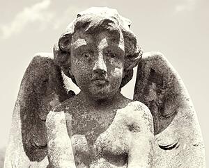 Sepia statue of cherub in graveyard looking at viewer