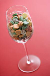 Wine glass full of colorful candy hearts with sayings on them on red background