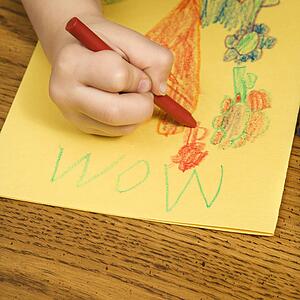 Boy drawing on yellow paper with crayons