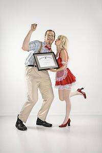 Young man dressed like nerd cheering and receiving kiss and certificate from young blonde woman dressed in french maid outfit