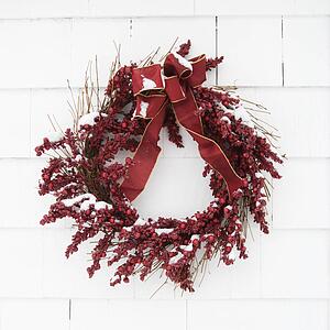 Red wreath covered in snow hanging on a white brick wall