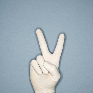 Hand wearing white rubber glove making a gesture meaning peace