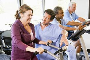 Nurse With Patient In Rehabilitation Using Exercise Machine