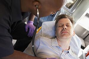 Paramedic using stethoscope on patient in ambulance
