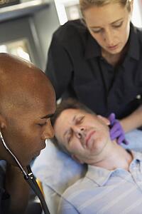 Paramedic using stethoscope on patient in ambulance