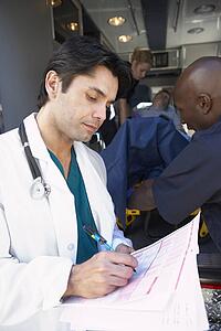 Doctor taking notes as paramedics unload patient