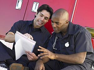 Two paramedics cheerfully doing paperwork, sitting by their ambulance
