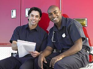Two paramedics cheerfully doing paperwork, sitting by their ambulance