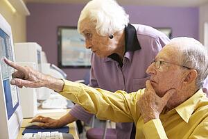 Senior woman helping senior man use computer