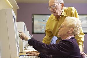 Senior man helping senior woman to use computer