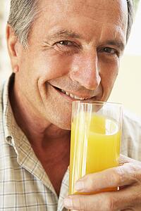 Senior Man Smiling At Camera And Drinking Orange Juice