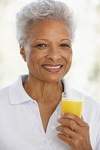 Senior Adult Holding A Glass Of Fresh Orange Juice, Smiling At The Camera