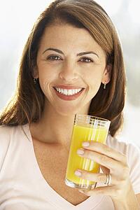 Mid Adult Woman Holding A Glass Of Orange Juice, Smiling At The Camera