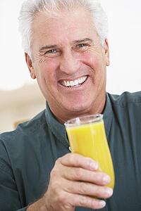 Senior Man Holding A Glass Of Fresh Orange Juice, Smiling At The Camera