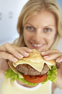 Mid Adult Woman Holding A Hamburger, Smiling At The Camera