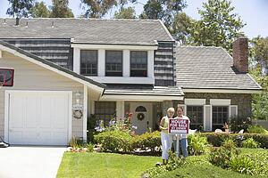 Couple Standing Outside House With Real Estate Sign