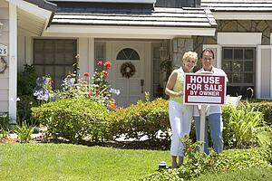 Couple Standing Outside House With Real Estate Sign