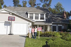 Family Standing Outside House With Real Estate Sign