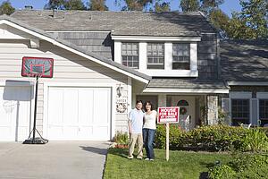 Couple Standing Outside House With Real Estate Sign