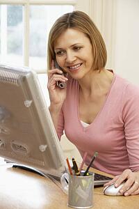Woman Using Computer And Talking On Phone
