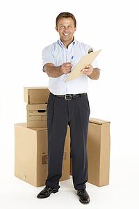 Portrait Of Courier Standing Next To Parcels, Holding A Clipboard