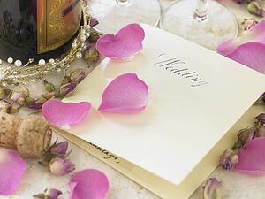 Wedding Invitation Next To Champagne Bottle Surrounded By Flower Petals