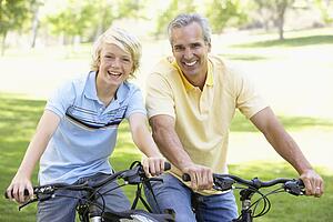 Father And Son Cycling Through A Park