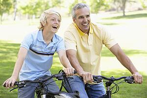 Father And Son Cycling Through A Park