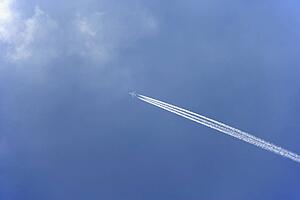 White Condensation Trail From A Commercial Airplane As It Flies Across A Blue Sky