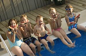 Group of children sitting by swimming pool eating watermelon