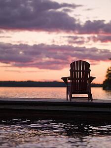 Lake of the Woods, Ontario, Canada; Empty deck chair on a pier next to a lake