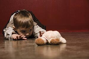 Toddler crawling on floor reaching for teddy bear