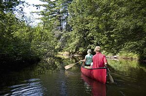 Muskokas, Ontario, Canada; couple canoeing down a river