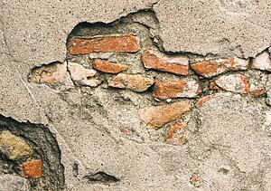 Broken wall revealing bricks beneath cement facing