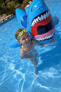 Girl playing in swimming pool with inflatable shark