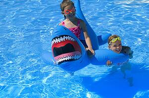 Girls playing in swimming pool with inflatable shark