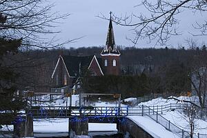 Christmas lights decorating a snow covered church and bridge