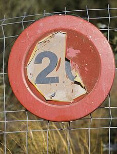 Old faded 20 kilometer per hour road sign on chain link fence