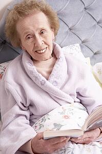 Senior Woman Relaxing In Bed With Book