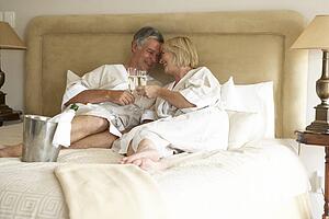 Middle Aged Couple Enjoying Champagne In Bedroom