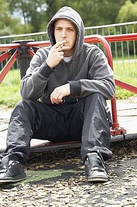 Young Man Sitting In Playground Smoking Joint