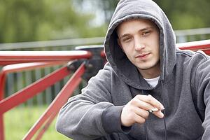 Young Man Sitting In Playground Smoking Joint