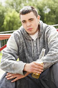 Young Man Sitting In Playground Drinking Beer